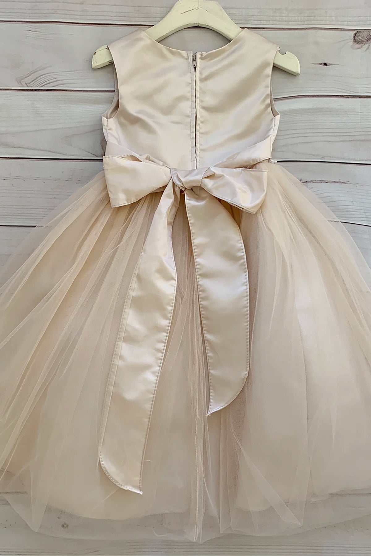 A sleeveless champagne tulle flower girl dress with a large satin bow at the waist.