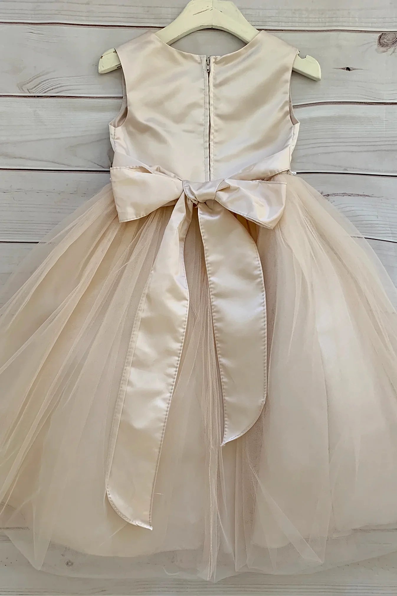 A sleeveless champagne tulle flower girl dress with a large satin bow at the waist.