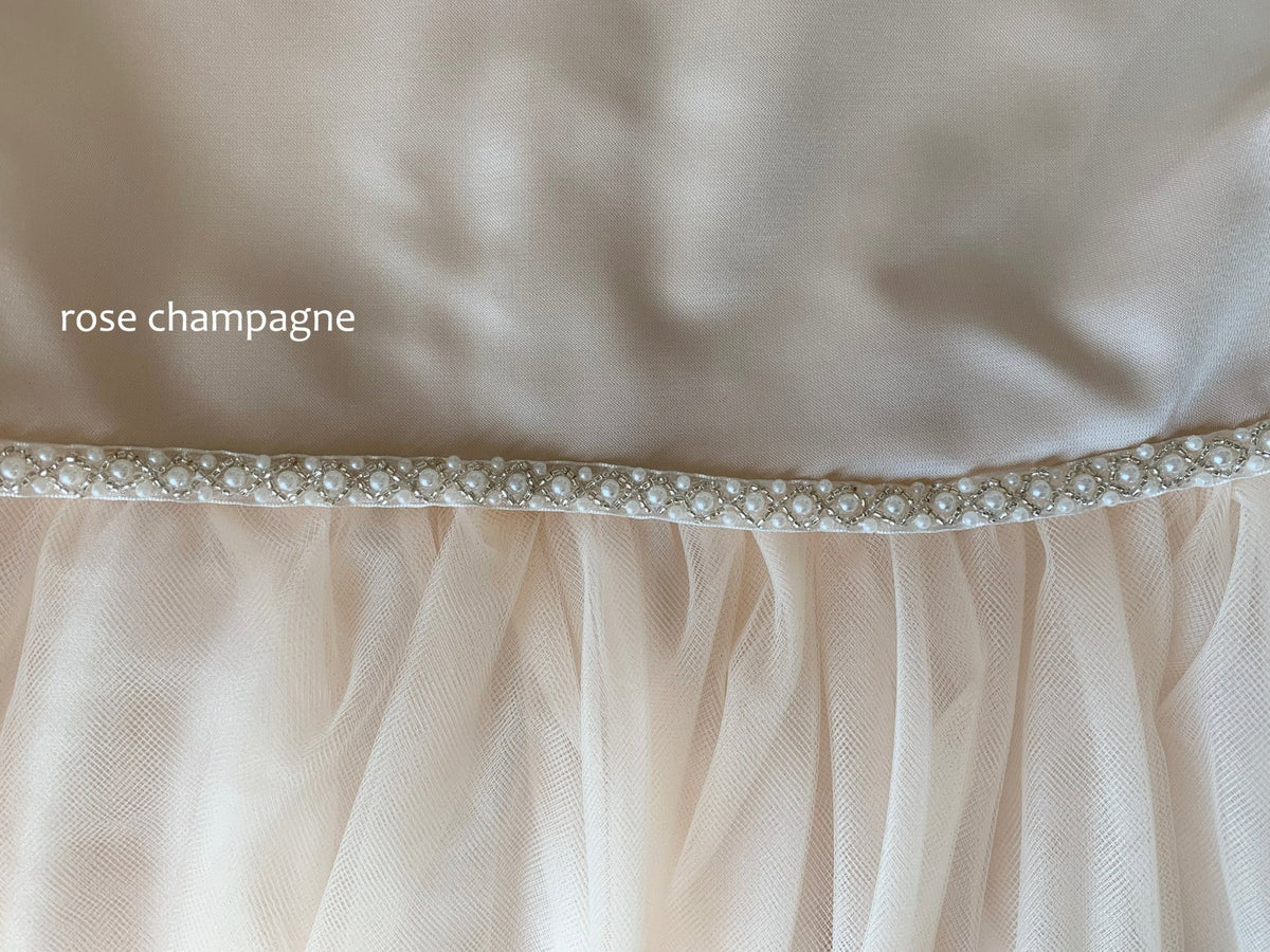 Close-up of a rose champagne-colored fabric with a decorative pearl trim. Flower girl dress.