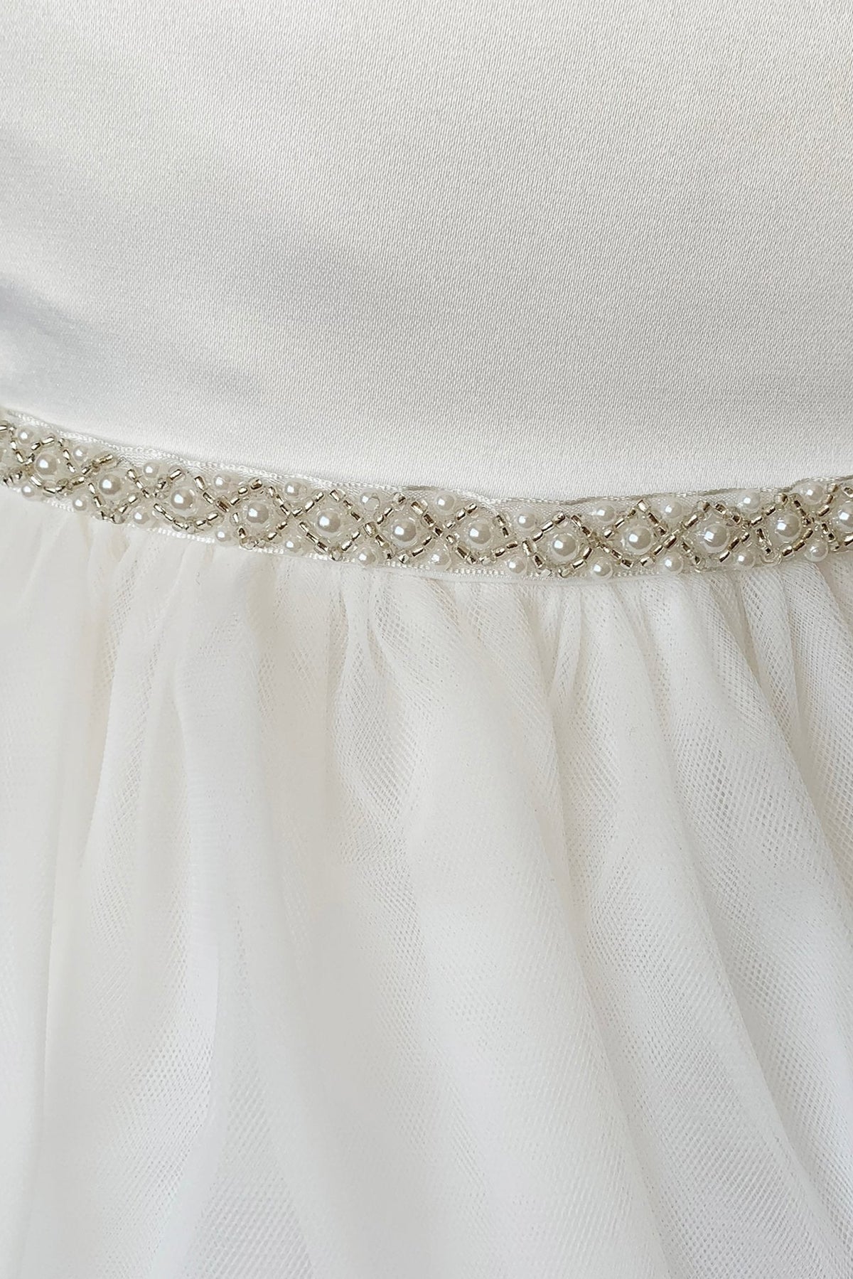 Close-up of an off white flower girl dress with a decorative ivory belt featuring pearls and crystals.
