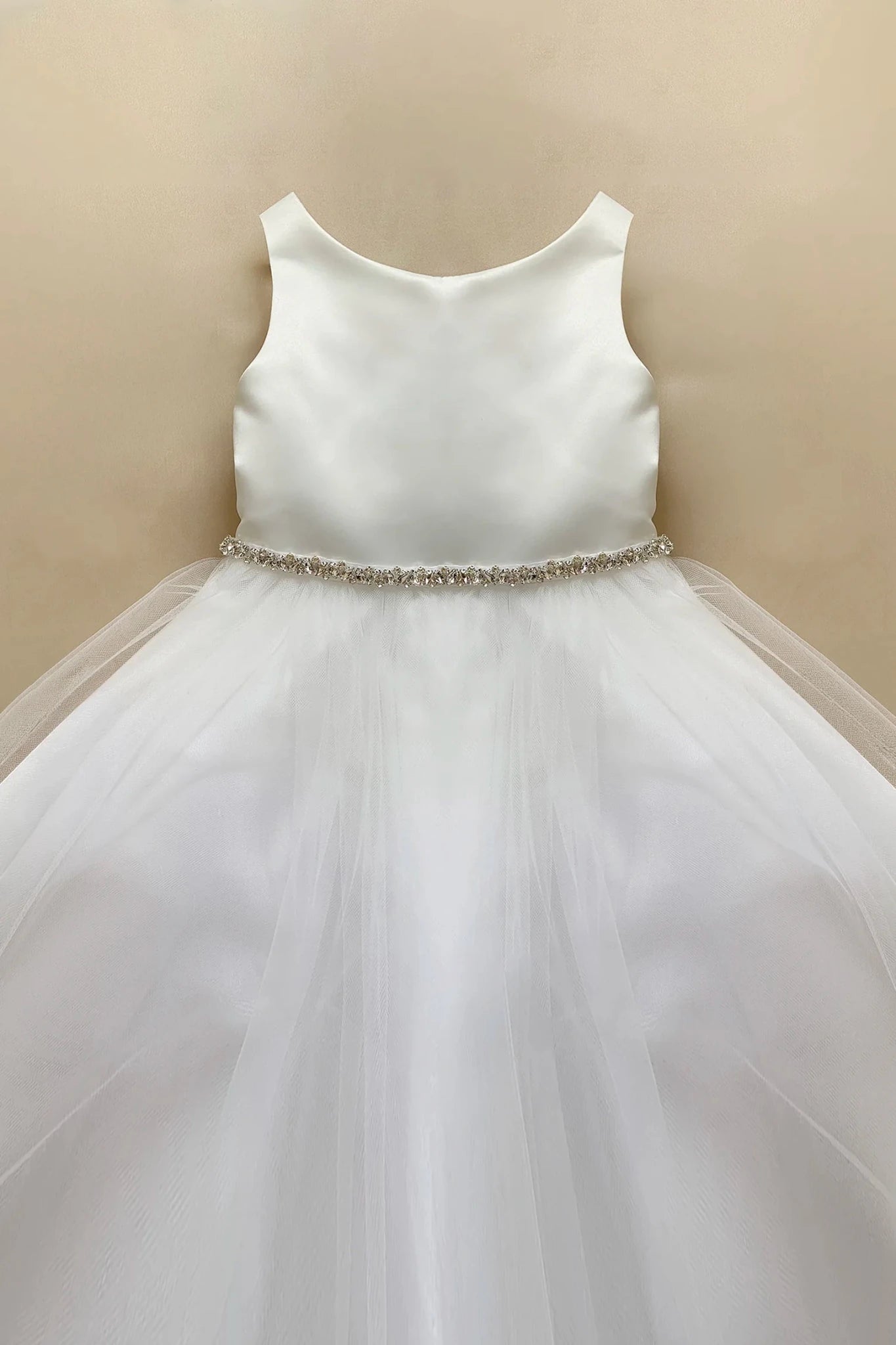 White sleeveless flower girl dress with a satin bodice, a rhinestone waistband, and a voluminous tulle skirt.