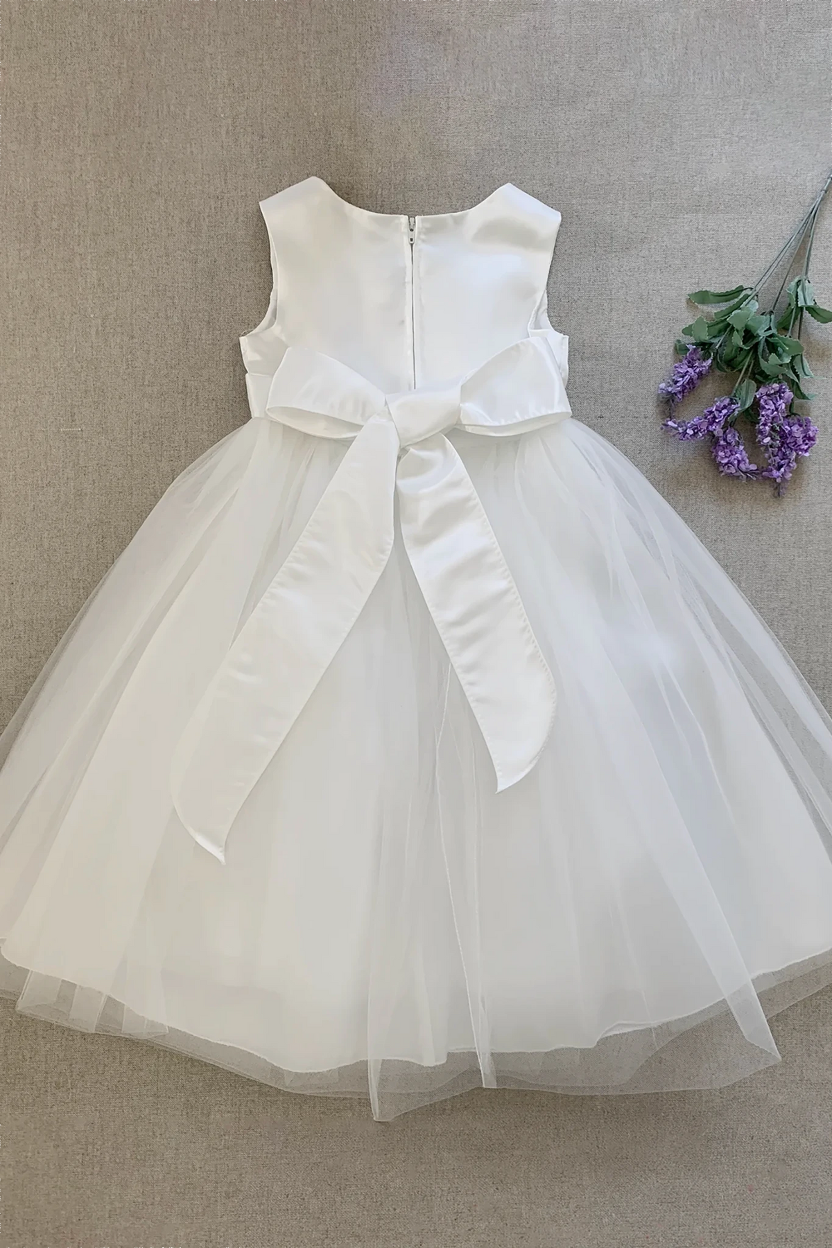 Refined styling highlights a sleeveless white kids tulle flower girl dress with a large satin bow at the waist.