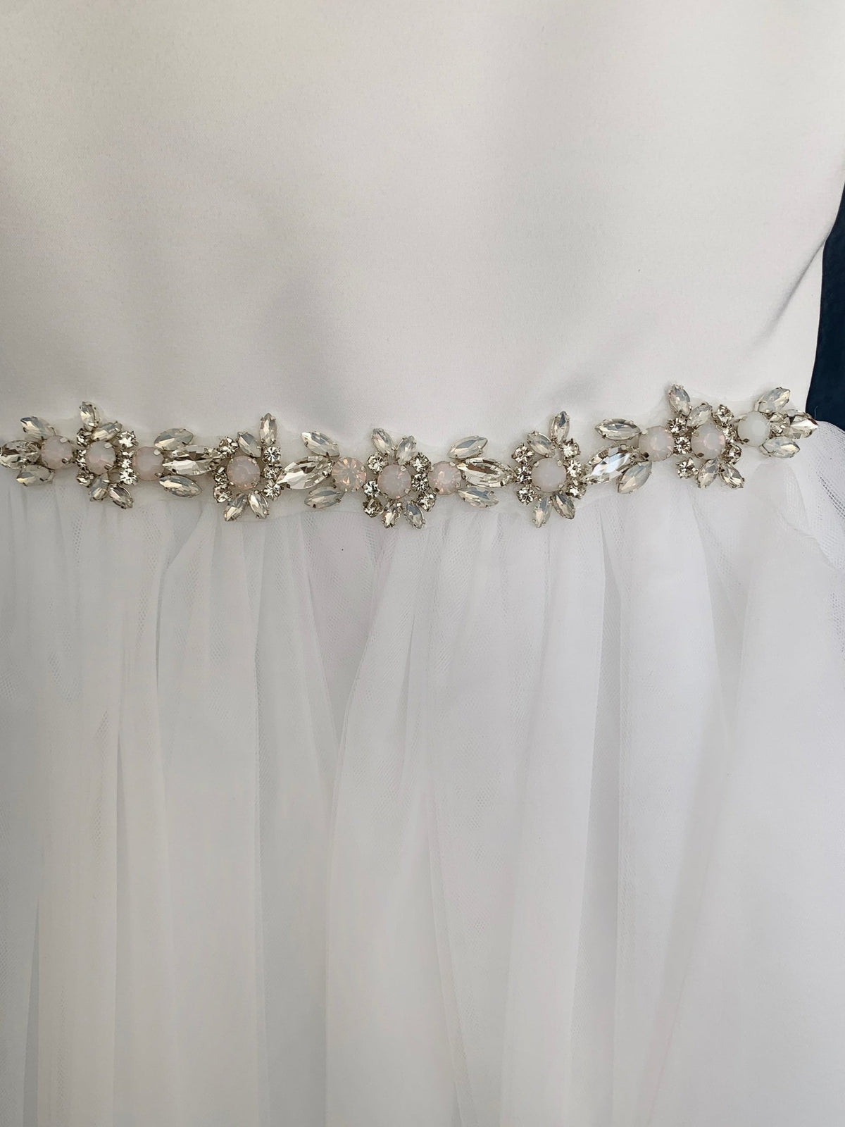 Close-up of a white flower girl dress with a decorative silver belt featuring crystals and pearls.