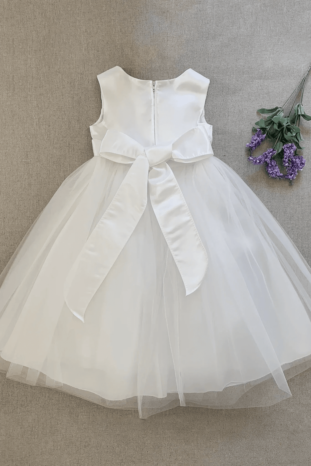 A sleeveless white kids tulle flower girl dress with a large satin bow at the waist.