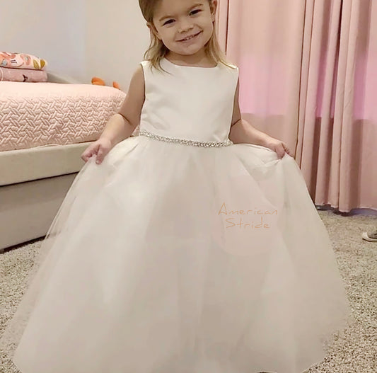 Young girl in a white dress with 'Avery' embroidered on it, sitting on a carpeted floor.