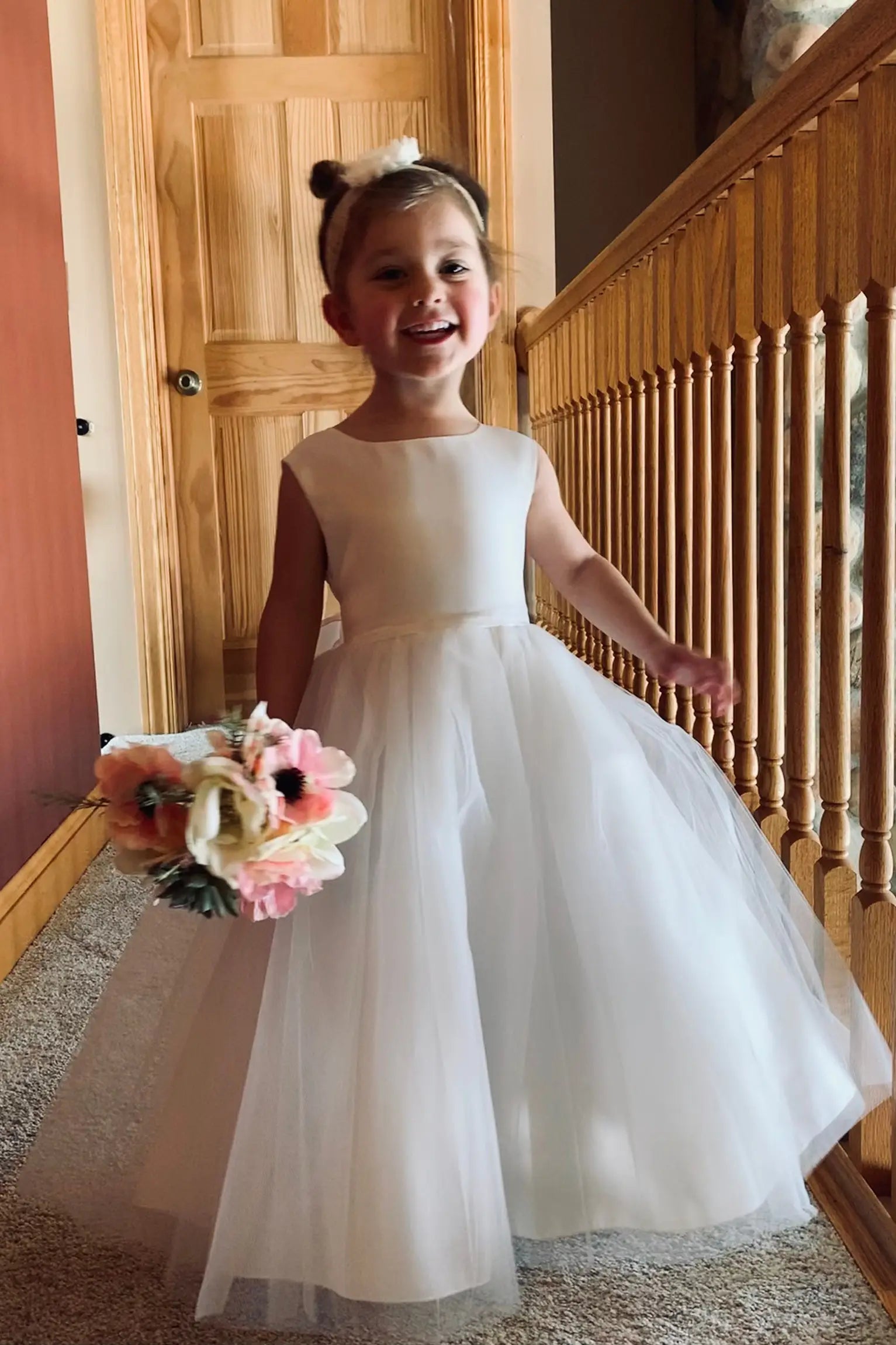 Young girl in a white satin top and tulle skirt dress holding flowers indoors. the dress is ankle length dress