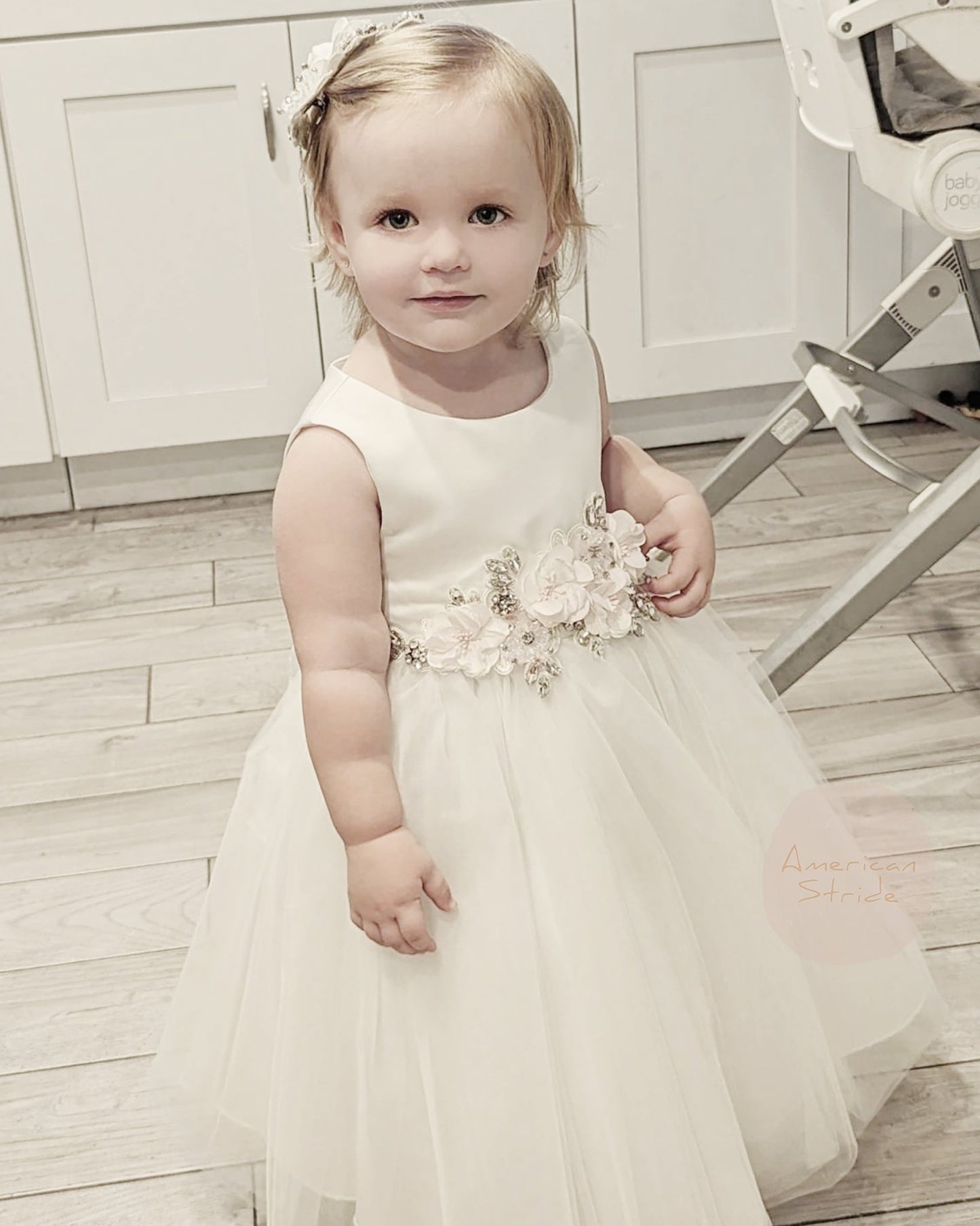 Young girl in a white dress with floral details standing on a wooden floor.