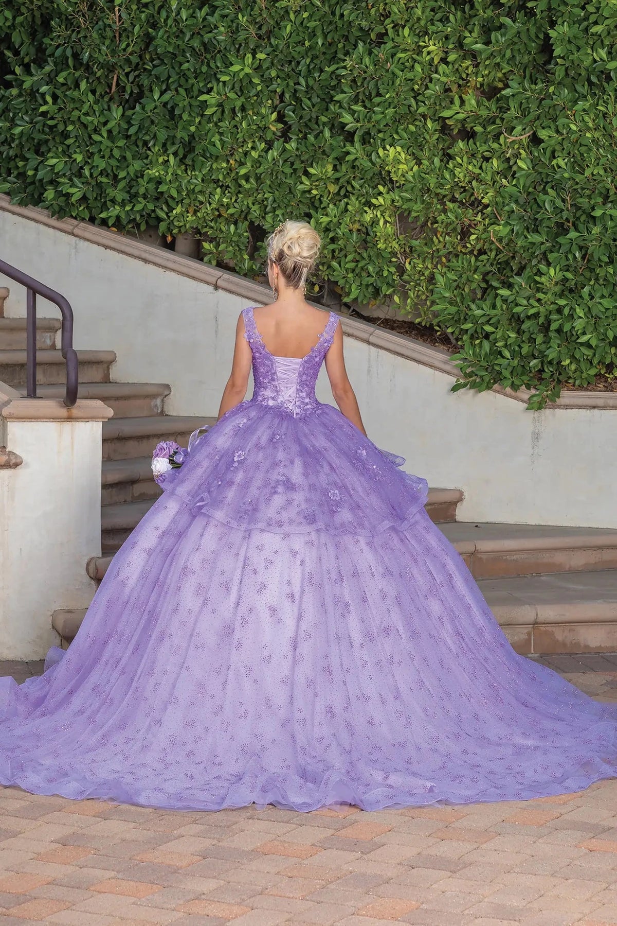 Back view of a Lilac quinceañera gown showing lace-up back, sheer cape, and floral appliqués