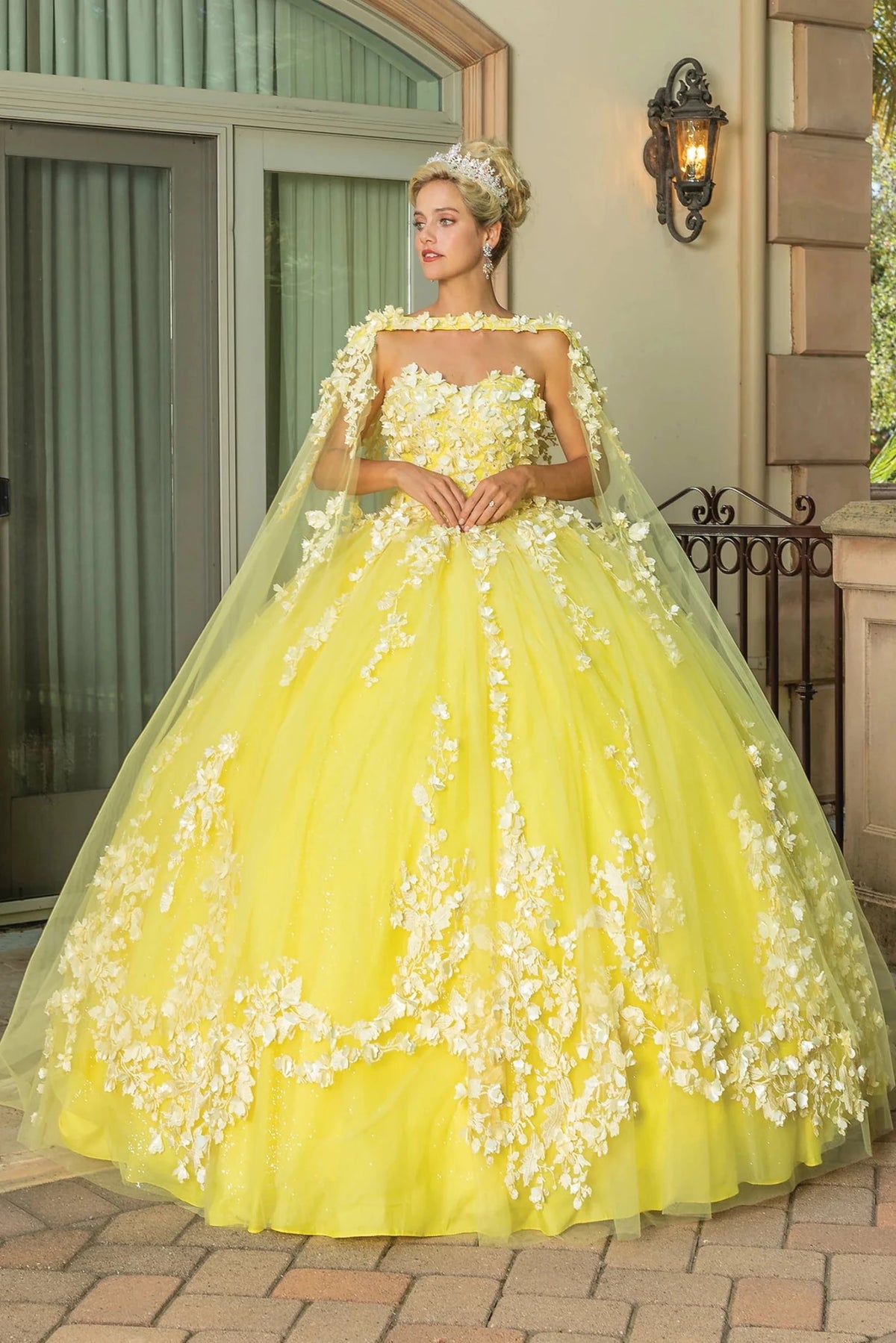 Front view of a Yellow quinceañera gown with strapless neckline, floral appliqués, and layered tulle skirt