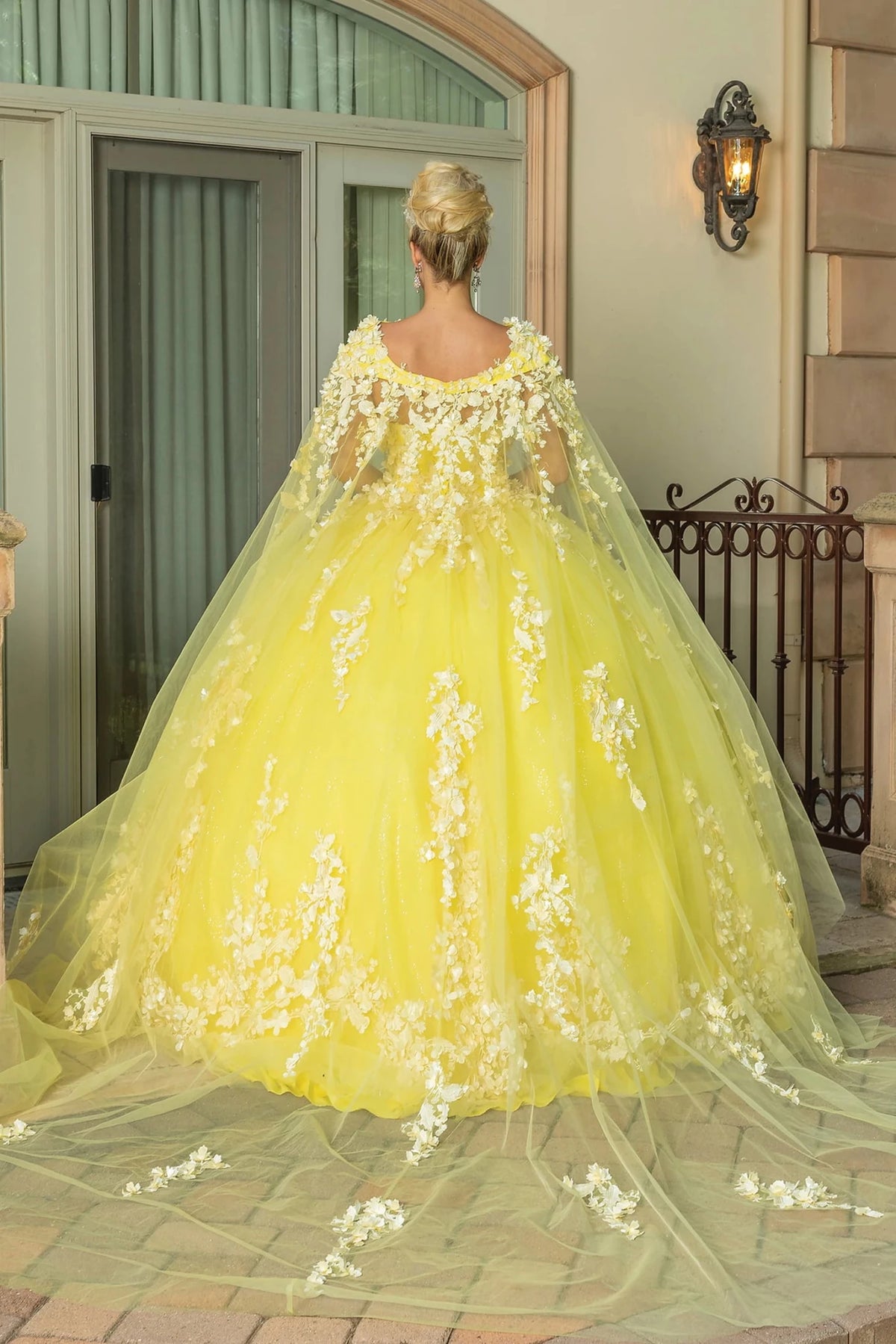 Back view of a Yellow quinceañera gown showing lace-up back, layered tulle skirt, and floral appliqués