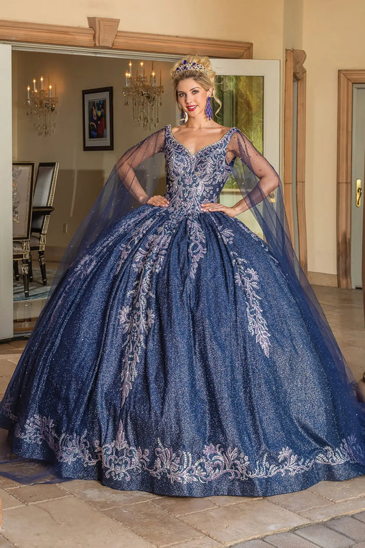 Full front view of a woman wearing a navy quinceañera dress with illusion V-neckline, embroidered bodice, sheer long cape sleeves, and glitter tulle ball gown skirt