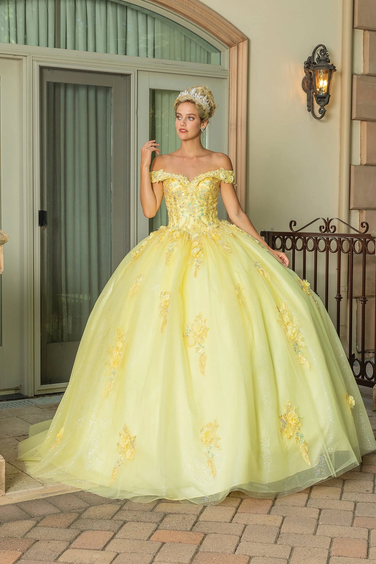 Showing floral appliqués scattered over its glitter tulle skirt, this Yellow quinceañera ball gown is shown in full view.