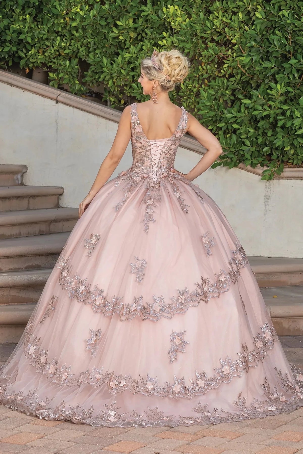 Back view of a Rose Gold quinceañera gown showing lace-up back, layered tulle skirt, and floral appliqués
