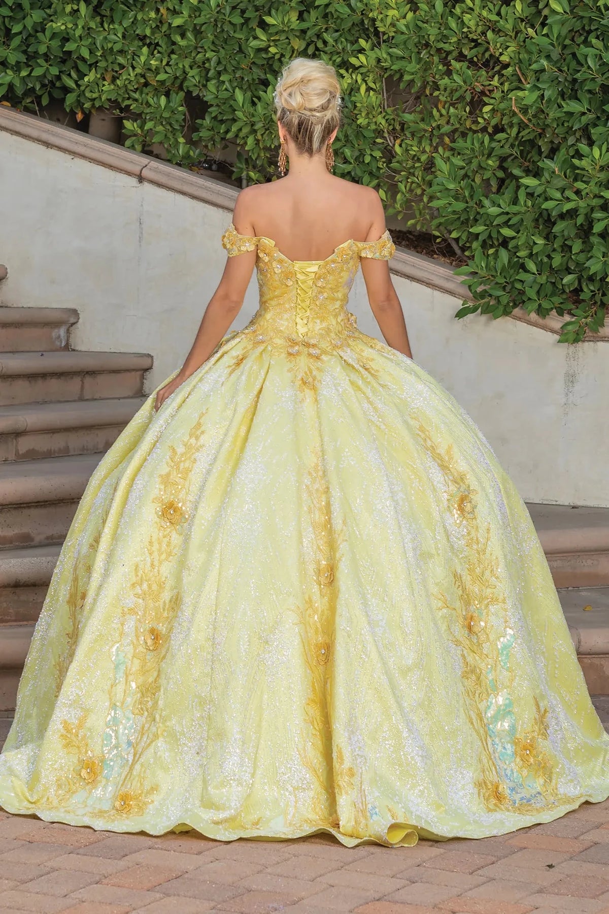Back view of a Yellow quinceañera gown showing lace-up back, glitter tulle skirt, and floral appliqués