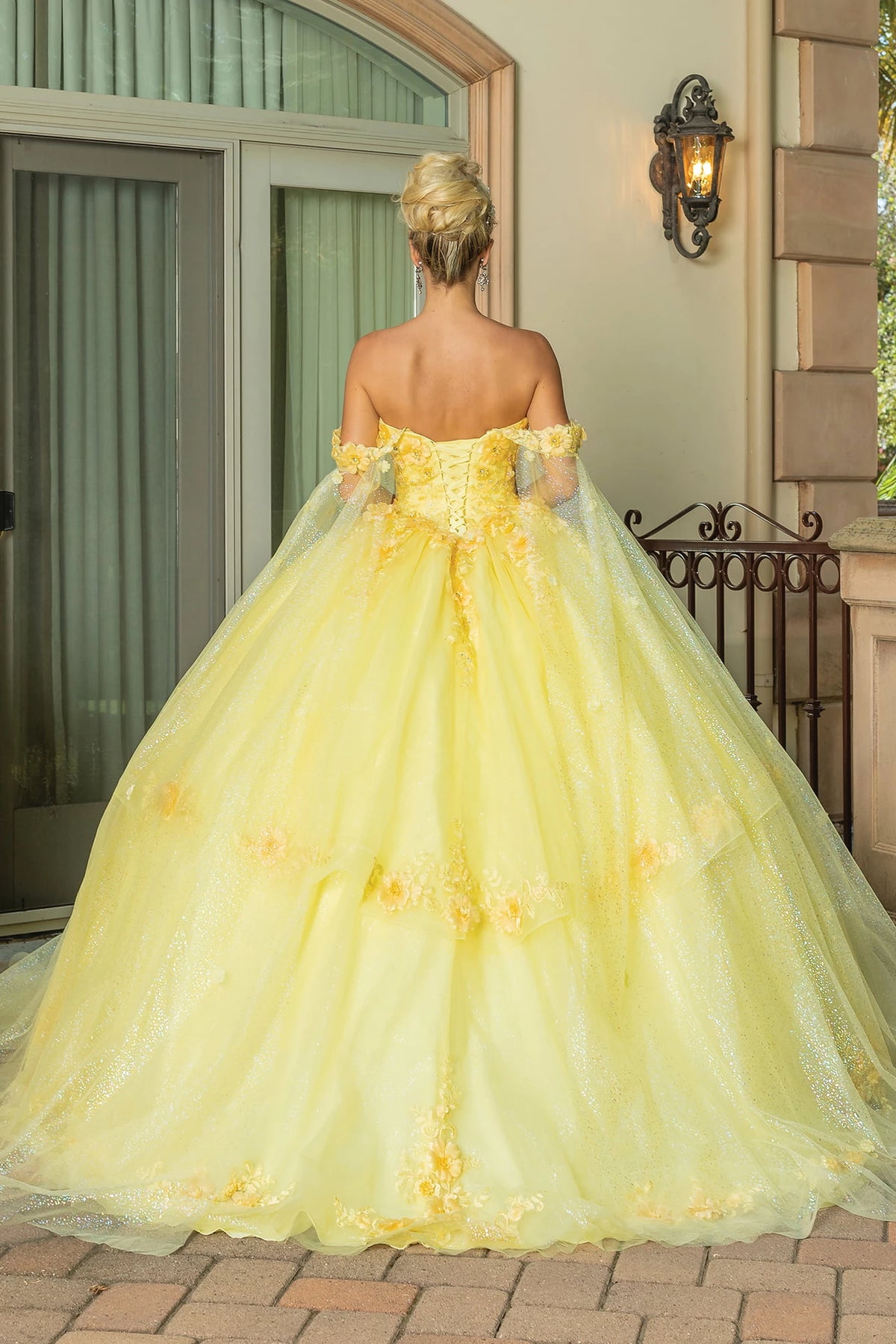 Revealing corset lacing and floral skirt accents, this Yellow quinceañera ball gown is shown from the back.