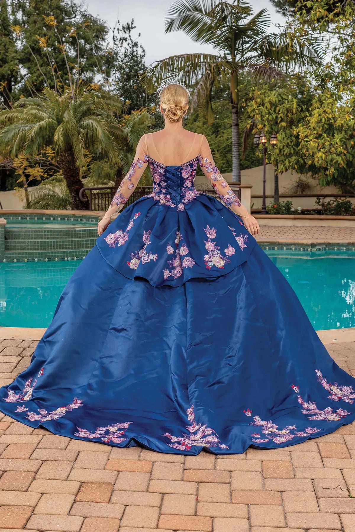 Back view of a Navy quinceañera gown showing lace-up back, sheer long sleeves, and flowing train
