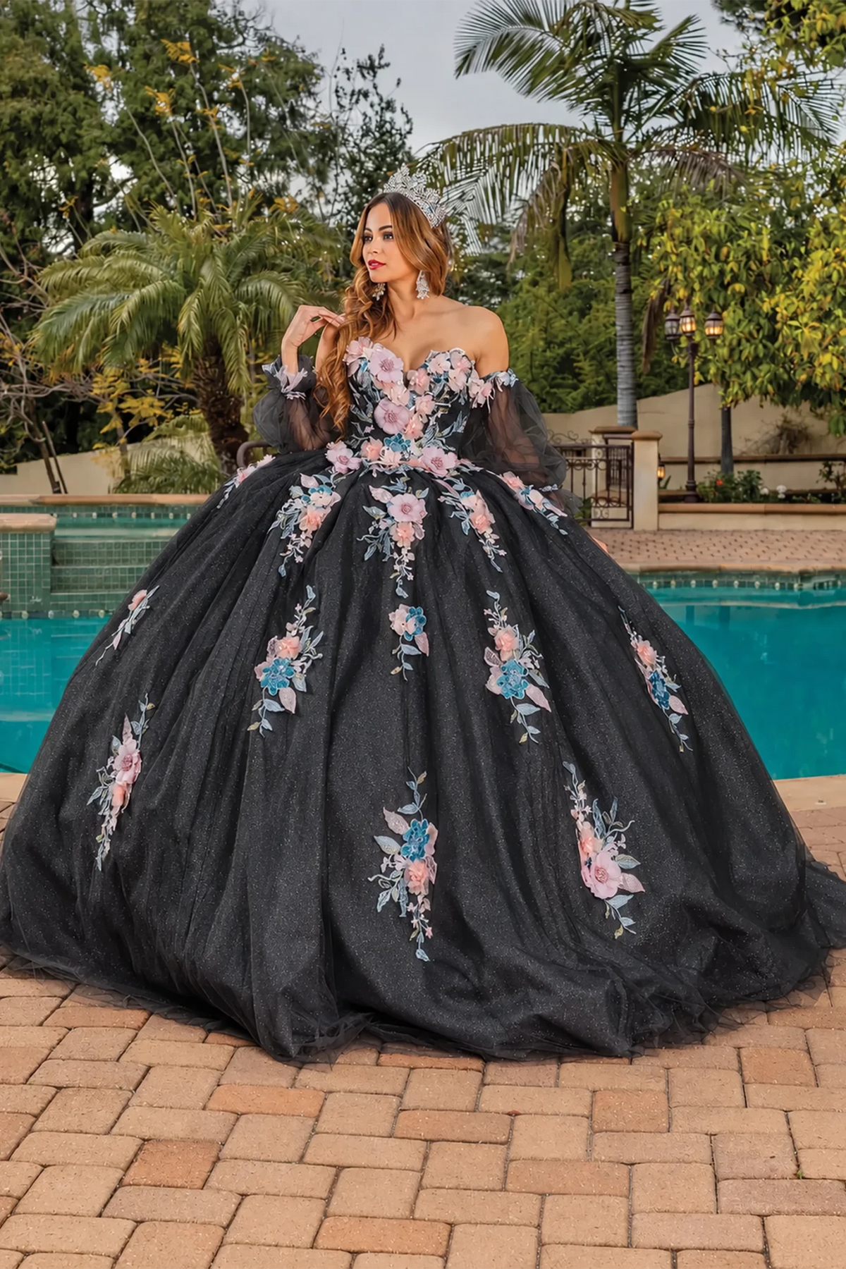 black quinceanera dress with large pink, blue, and white floral appliqués and sheer black sleeves.
