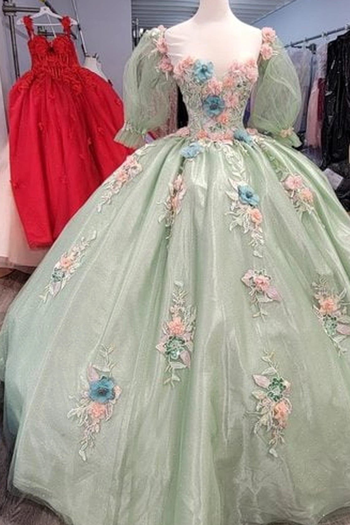 Front view of a Sage quinceañera gown with sheer sleeves, floral appliqués, and voluminous full skirt