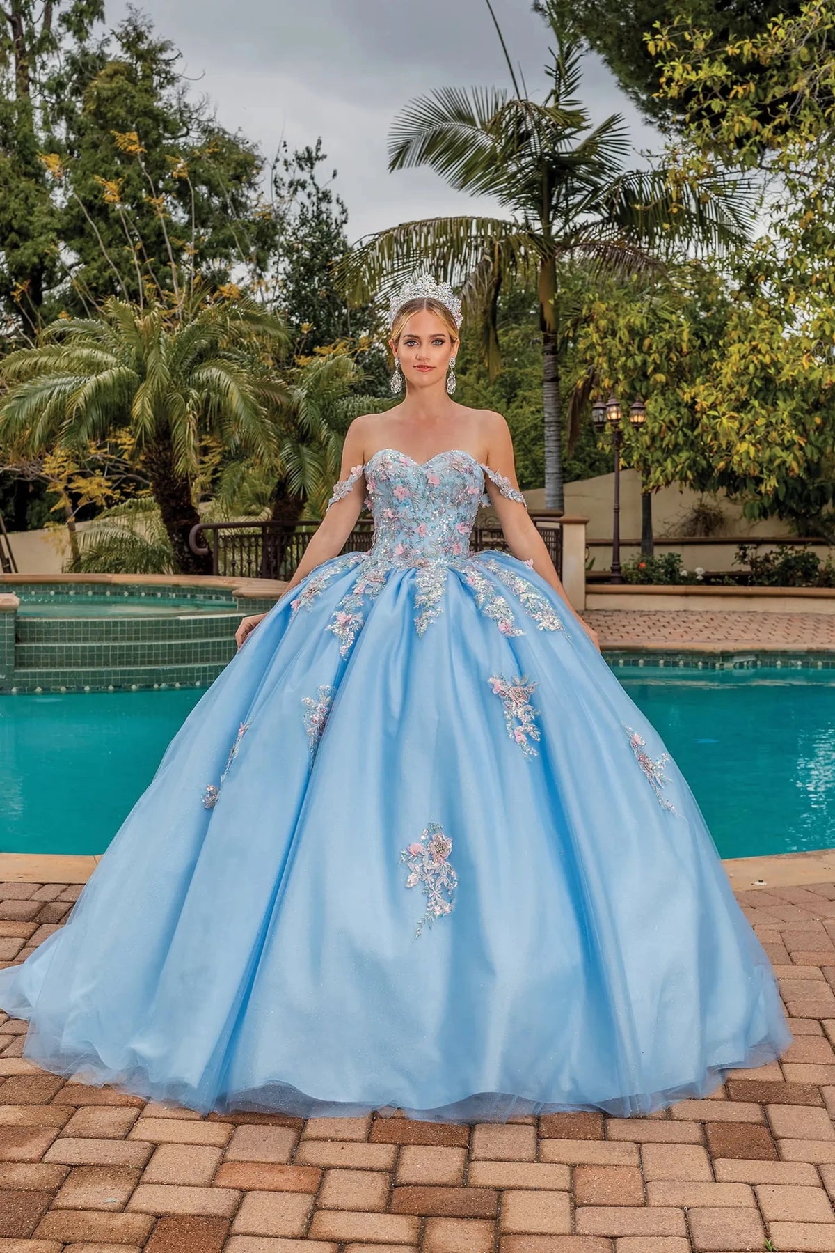Front view of a Bahama Blue quinceañera gown with sheer sleeves, embellished bodice, and crystal accents