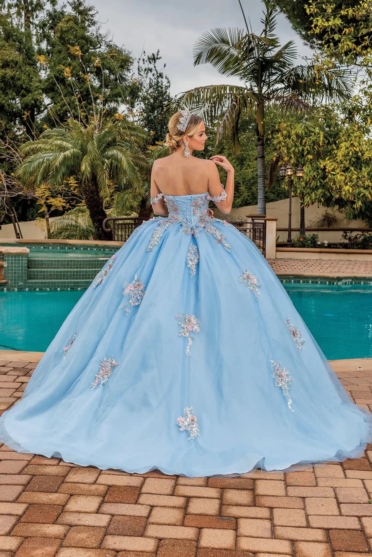 Back view of a Bahama Blue quinceañera gown showing lace-up back, sheer sleeves, and crystal accents
