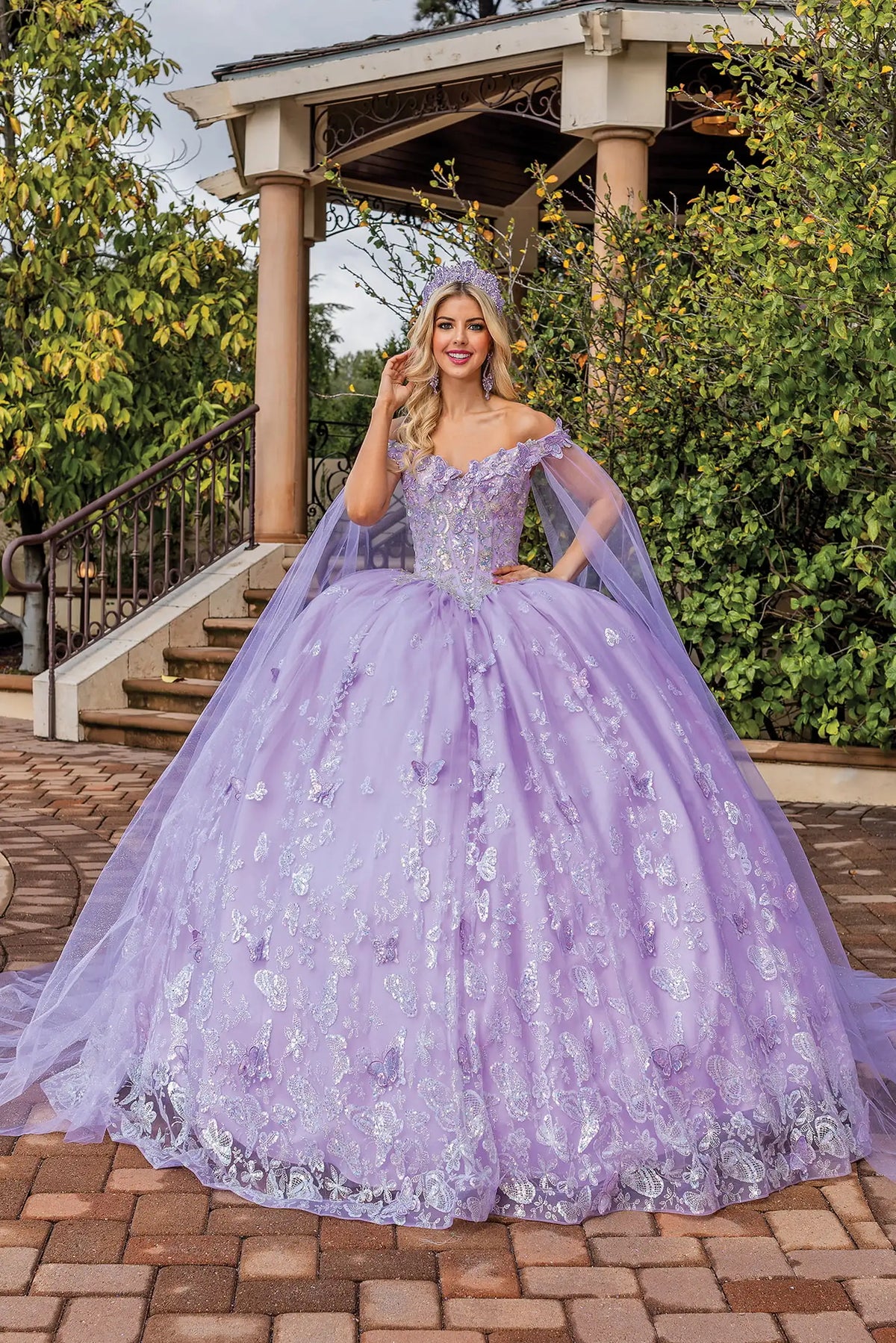 Showing floral appliqués and sheer shoulder drapes, this Lilac quinceañera ball gown is shown in full view.