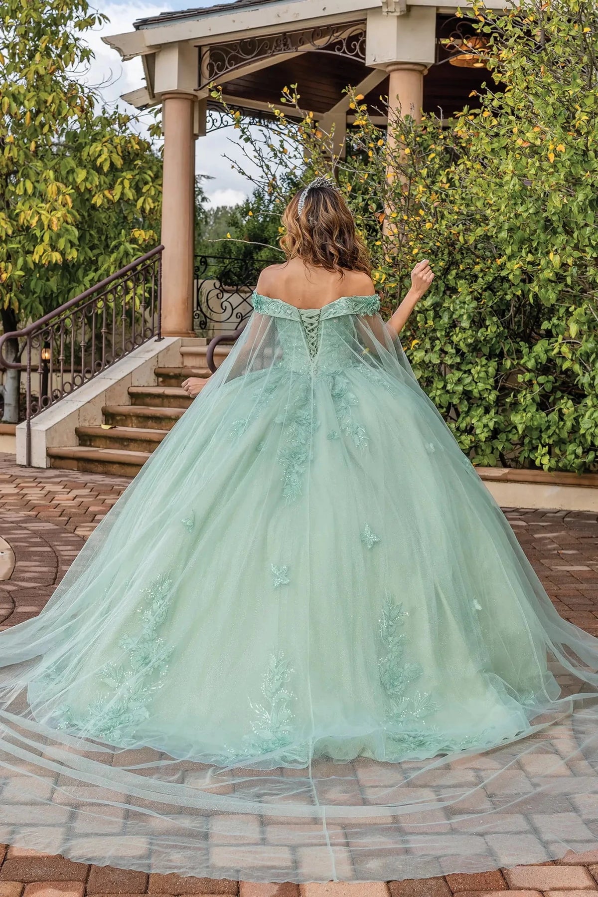 Back view of a Sage quinceañera gown showing lace-up back, sheer long cape, and floral embroidery