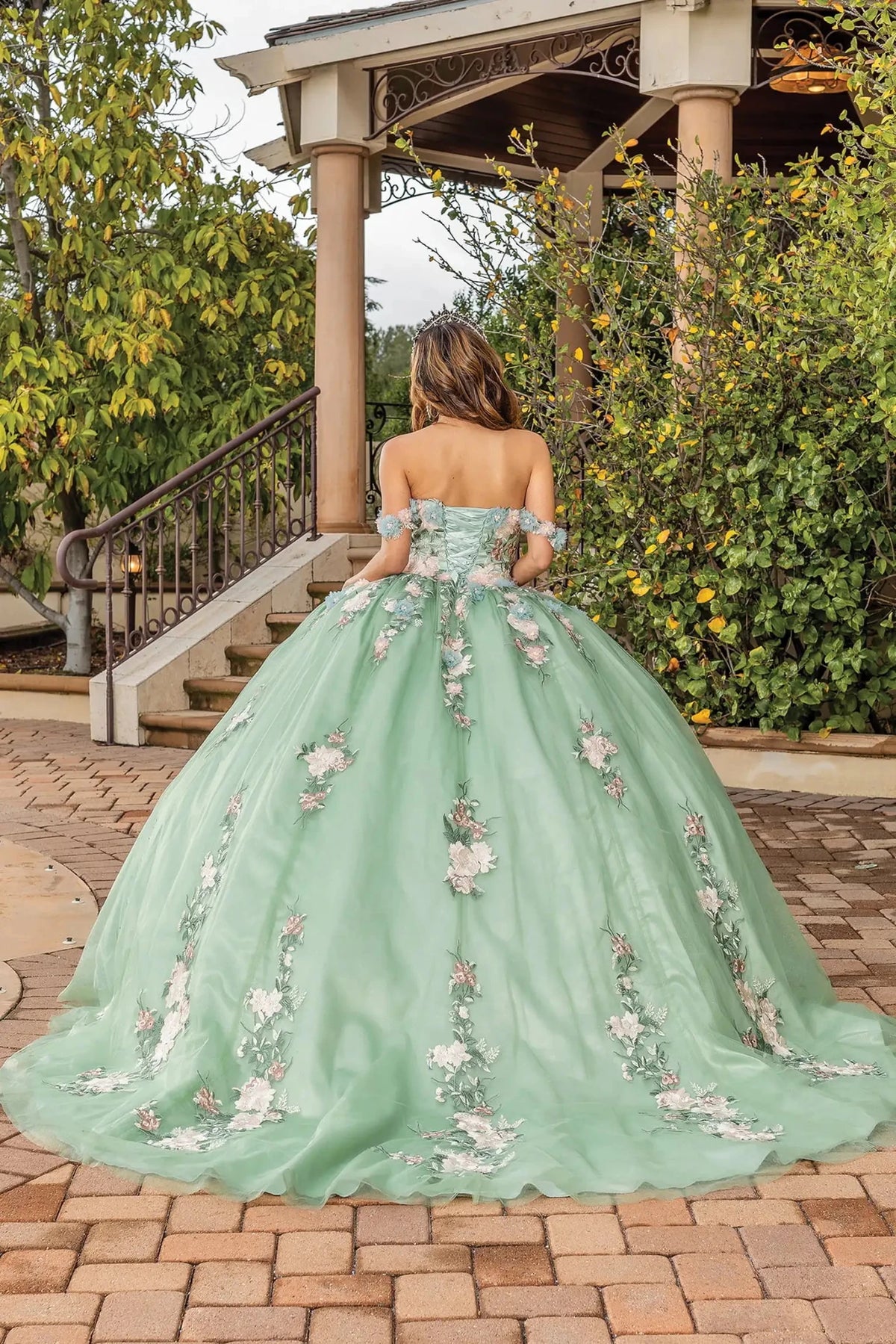 Back view of a Sage quinceañera gown showing lace-up back, scalloped hemline, and floral appliqués
