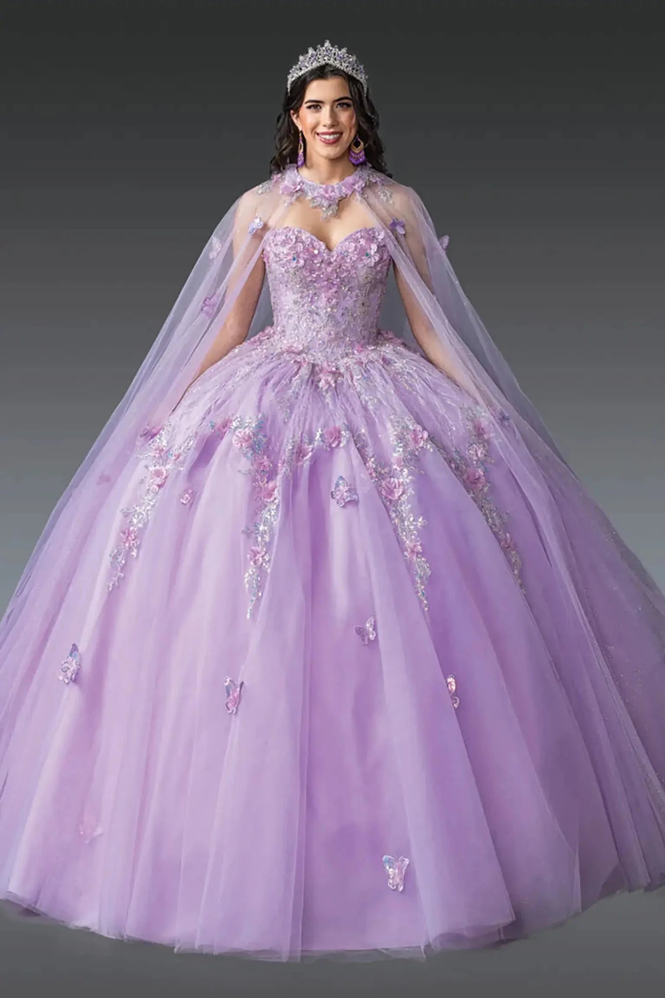 Front view of a lilac quinceañera ball gown with sweetheart corset bodice, crystal embellishments, butterfly appliqués, sheer tulle cape overlay, and a voluminous skirt.