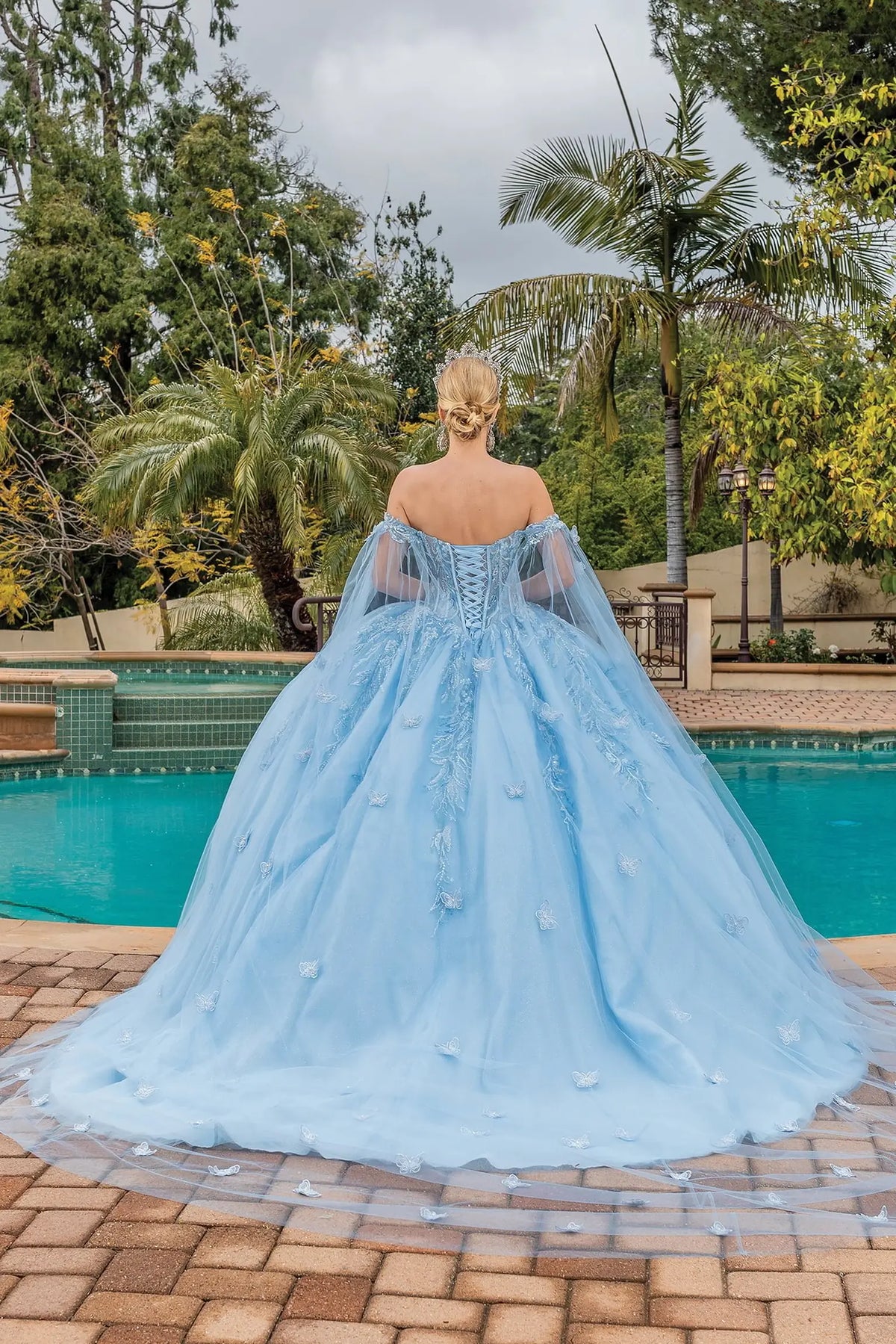 Back view of a Bahama Blue quinceañera gown showing lace-up back, sheer cape, and full tulle skirt
