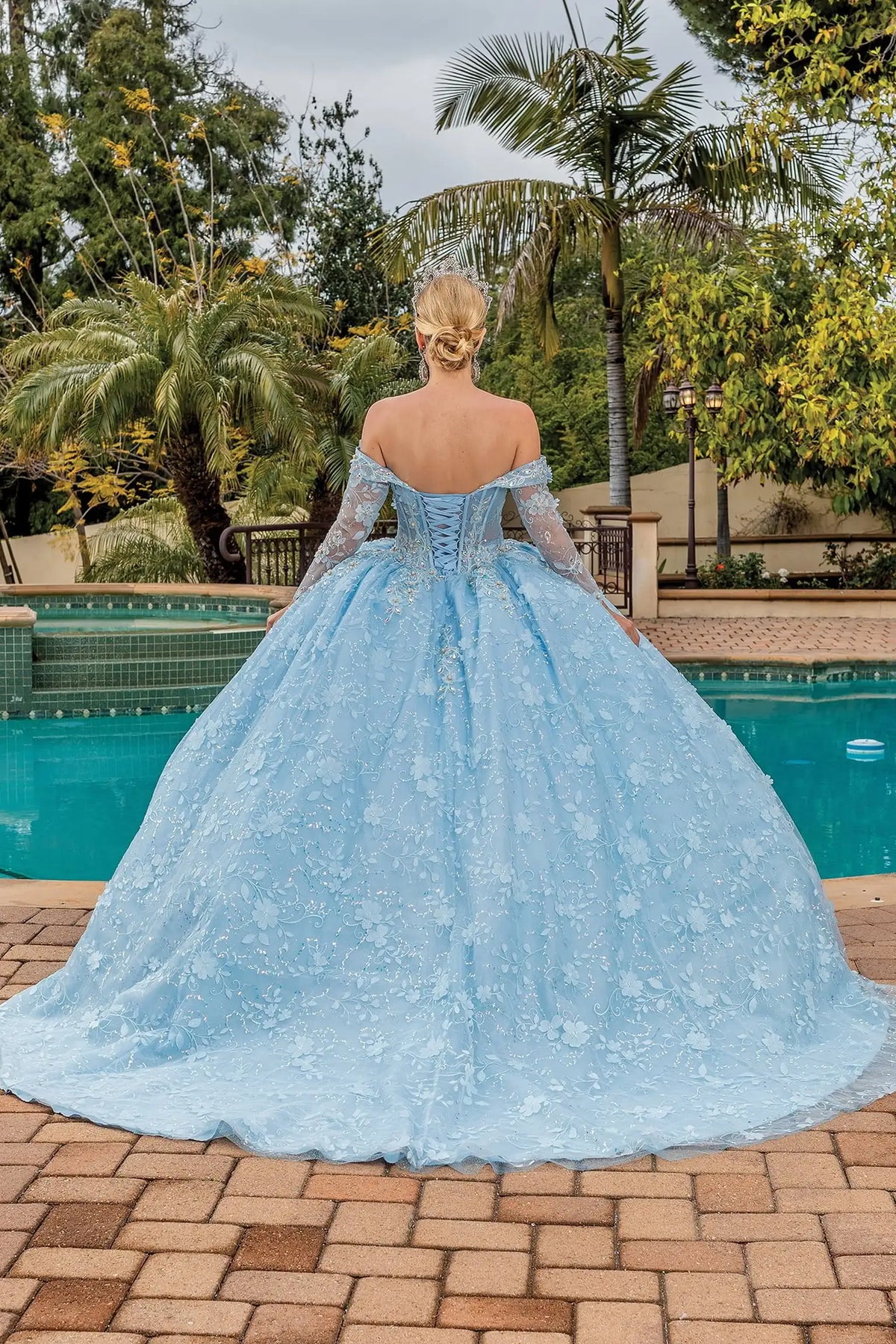 Back view of a Bahama Blue quinceañera gown showing lace-up back, long sleeves, and floral appliqués