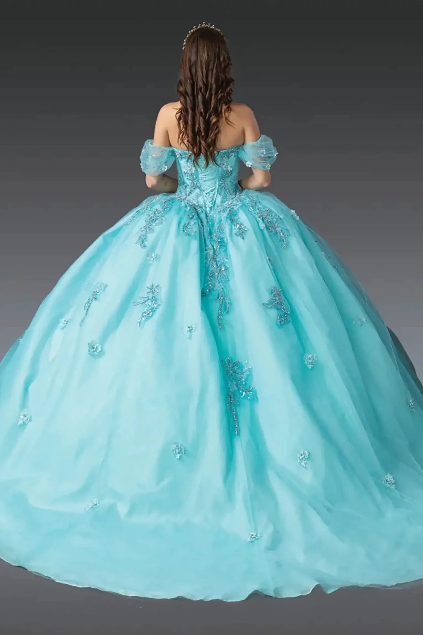Back view of aqua quinceañera ball gown showcasing lace-up corset back, off-shoulder puff sleeves, embroidered tulle skirt, and full ball gown silhouette photographed in studio lighting