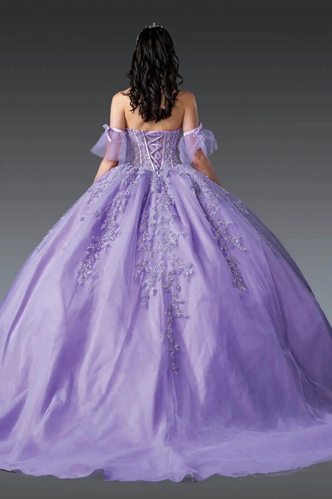 Back view of lilac quinceañera ball gown featuring lace-up corset back, off-shoulder tulle sleeves, floral appliqués, and voluminous tulle skirt