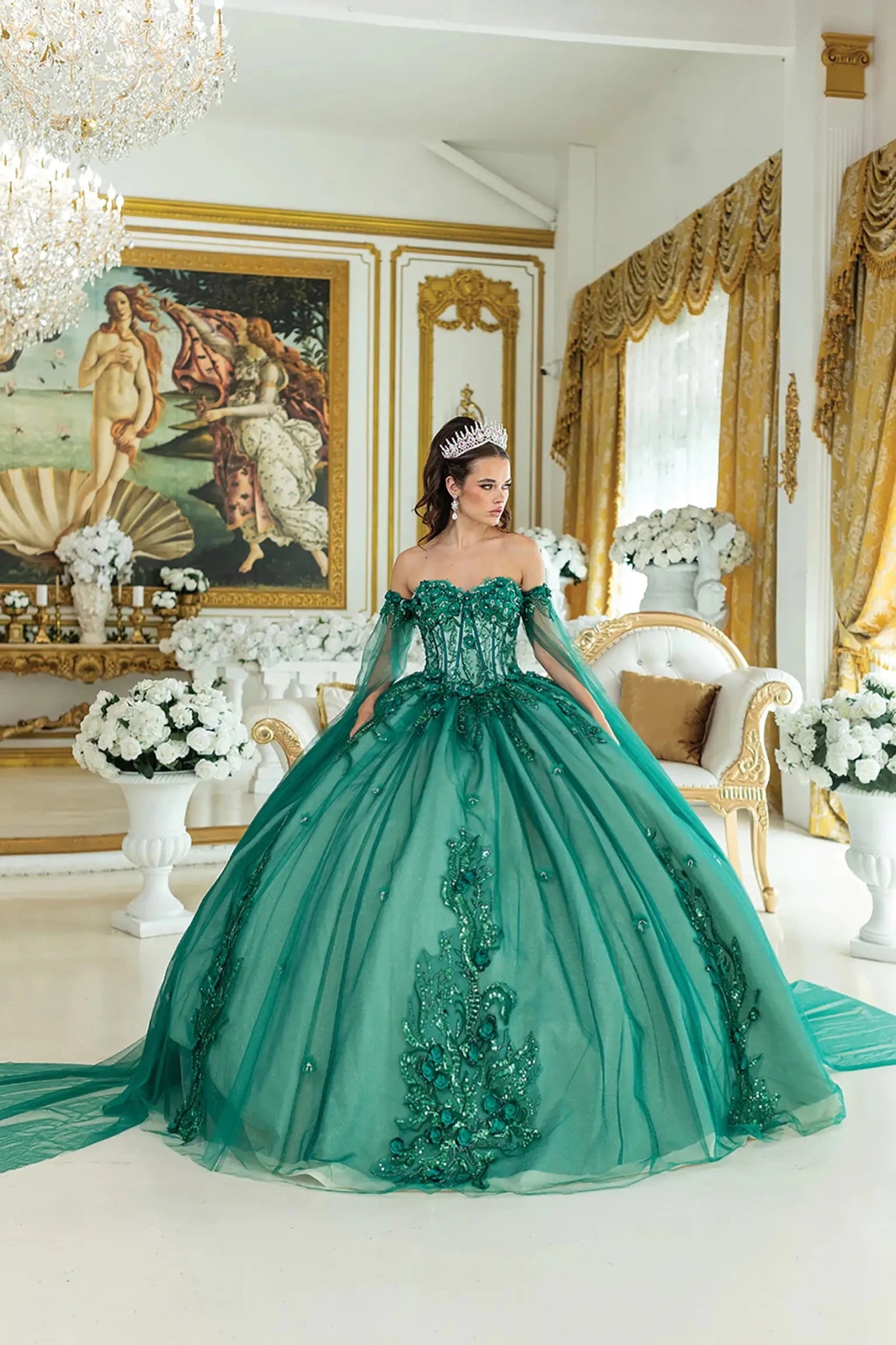 Woman standing front-facing in hunter green quinceañera ball gown with off-shoulder sleeves, beaded bodice, intricate embroidery, sheer cape details, floral accents, and voluminous tulle skirt