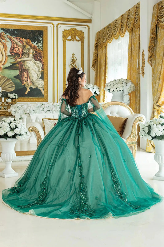 Woman standing back-facing in hunter green quinceañera ball gown with lace-up beaded bodice, off-shoulder sleeves, sheer cape with floral accents, and flowing tulle skirt with train