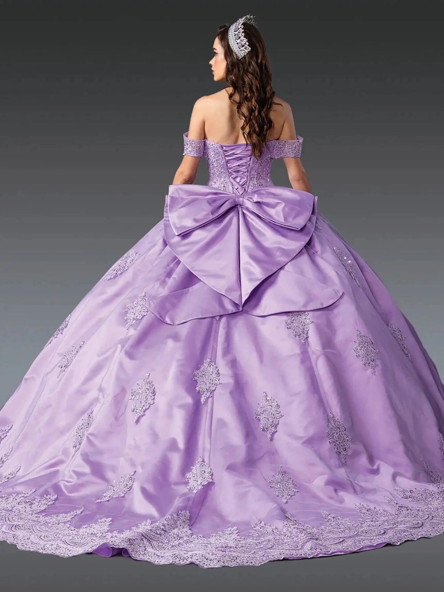Lilac quinceanera ball gown back view showing lace up corset back, oversized satin bow detail, embroidered skirt panels, and dramatic sweeping train