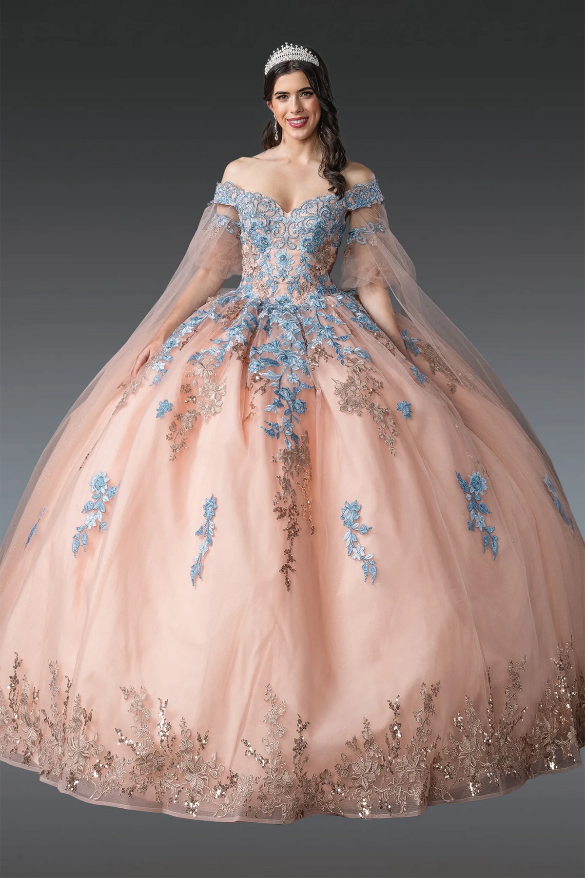 off-the-shoulder ball gown with a sheer tulle skirt in blush pink, decorated with blue floral embroidery and metallic sequined detailing