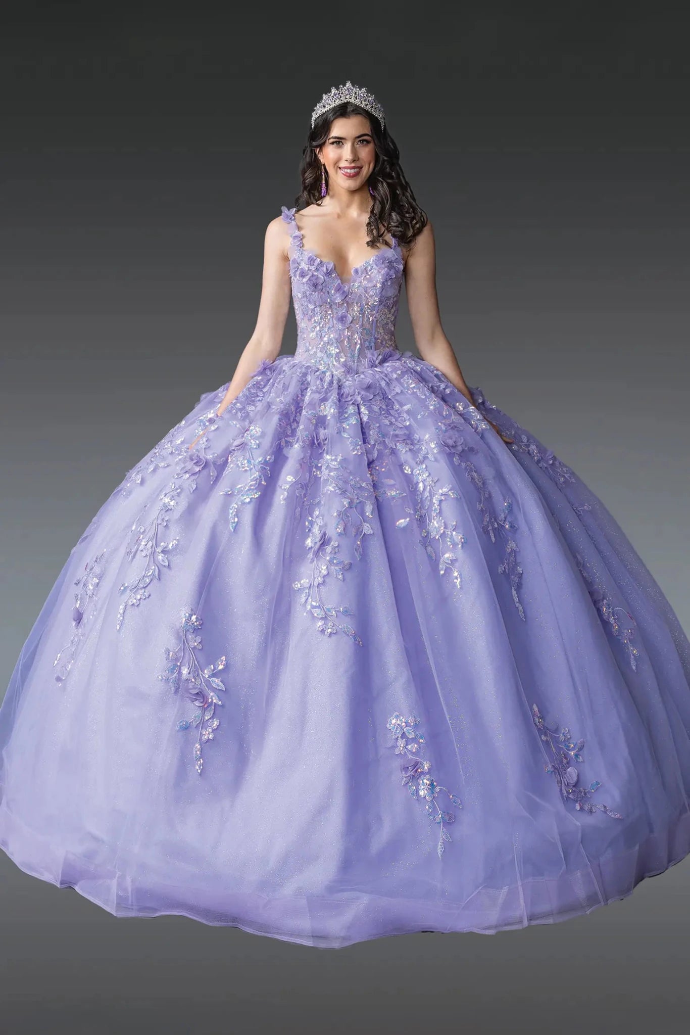 Woman standing front-facing in lilac quinceañera ball gown with deep V-neckline, embroidered floral details, sheer overlay, and voluminous layered skirt