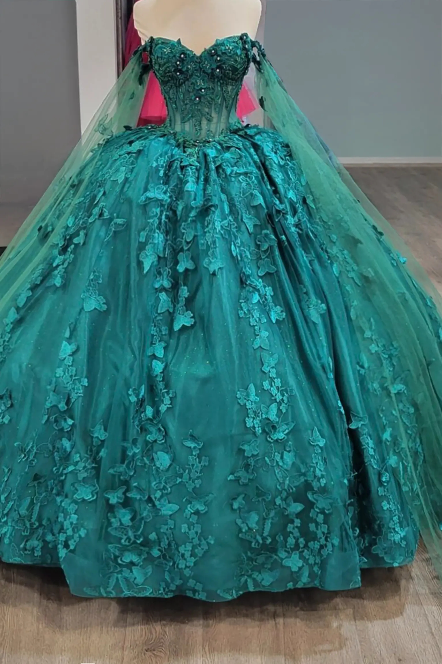 hunter green quinceanera dress with beaded bodice, floral embroidery, butterfly appliques, and sheer long sleeves cape