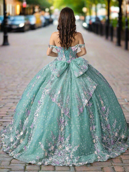 Woman standing back-facing in sage quinceañera ball gown with lace-up strapless bodice, embroidered floral accents, and flowing layered ruffled skirt with train