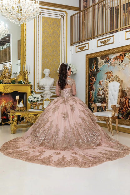 Woman standing back-facing in elegant rose gold quinceañera ball gown with lace overlay, lace-up bodice, sheer long sleeves, and flowing sparkling skirt with train