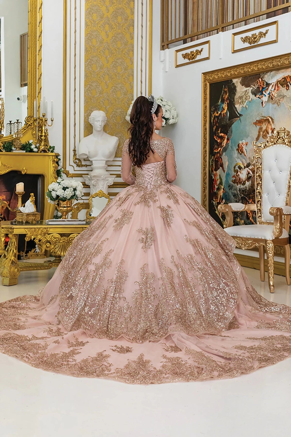 rose gold quinceañera ball gown with lace overlay, lace-up bodice, sheer long sleeves, and flowing sparkling skirt with train