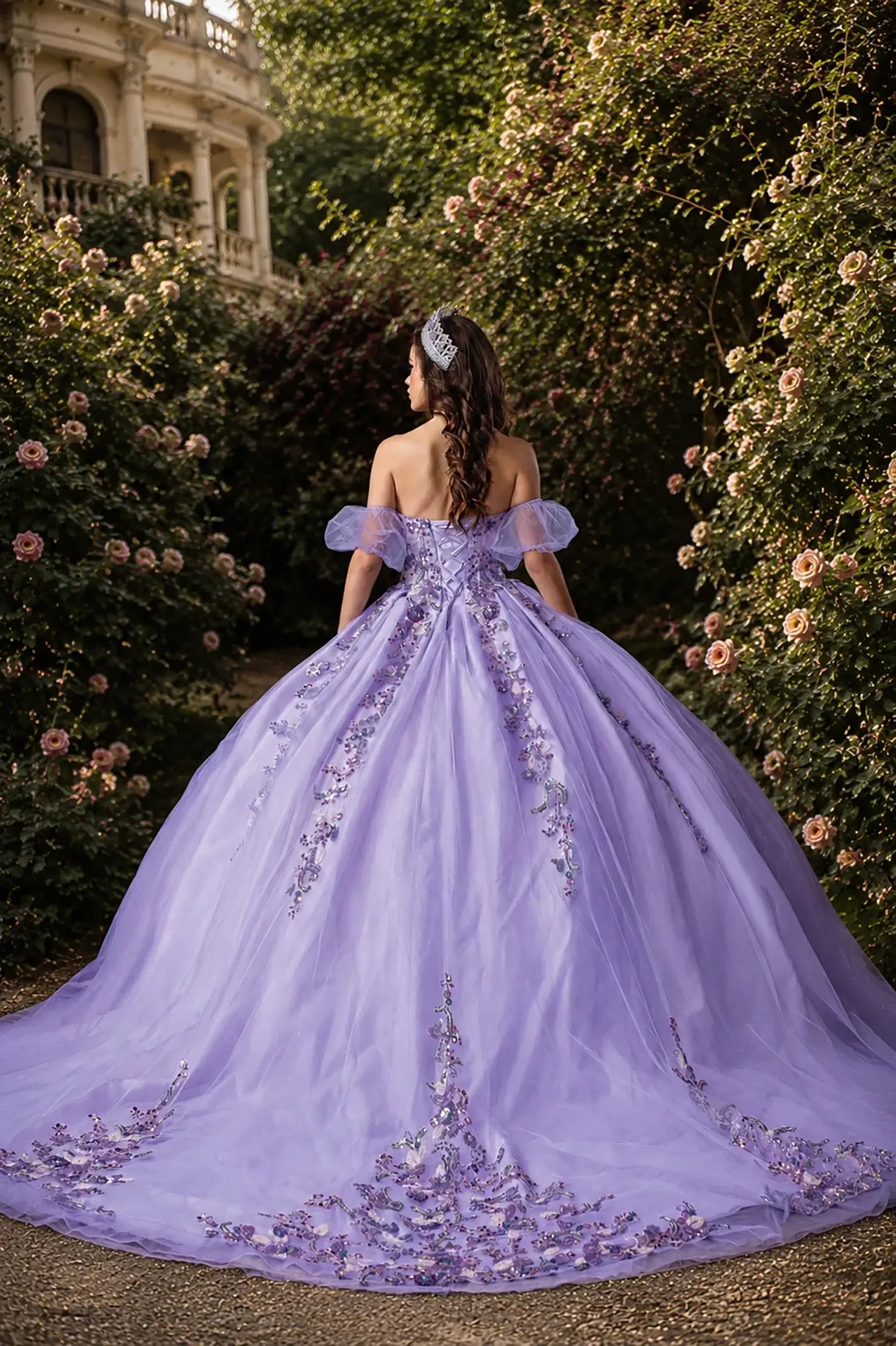 Back view of a lilac quinceanera dress with lace-up corset, floral appliques, glittered fabric, detachable puff sleeves, and layered skirt