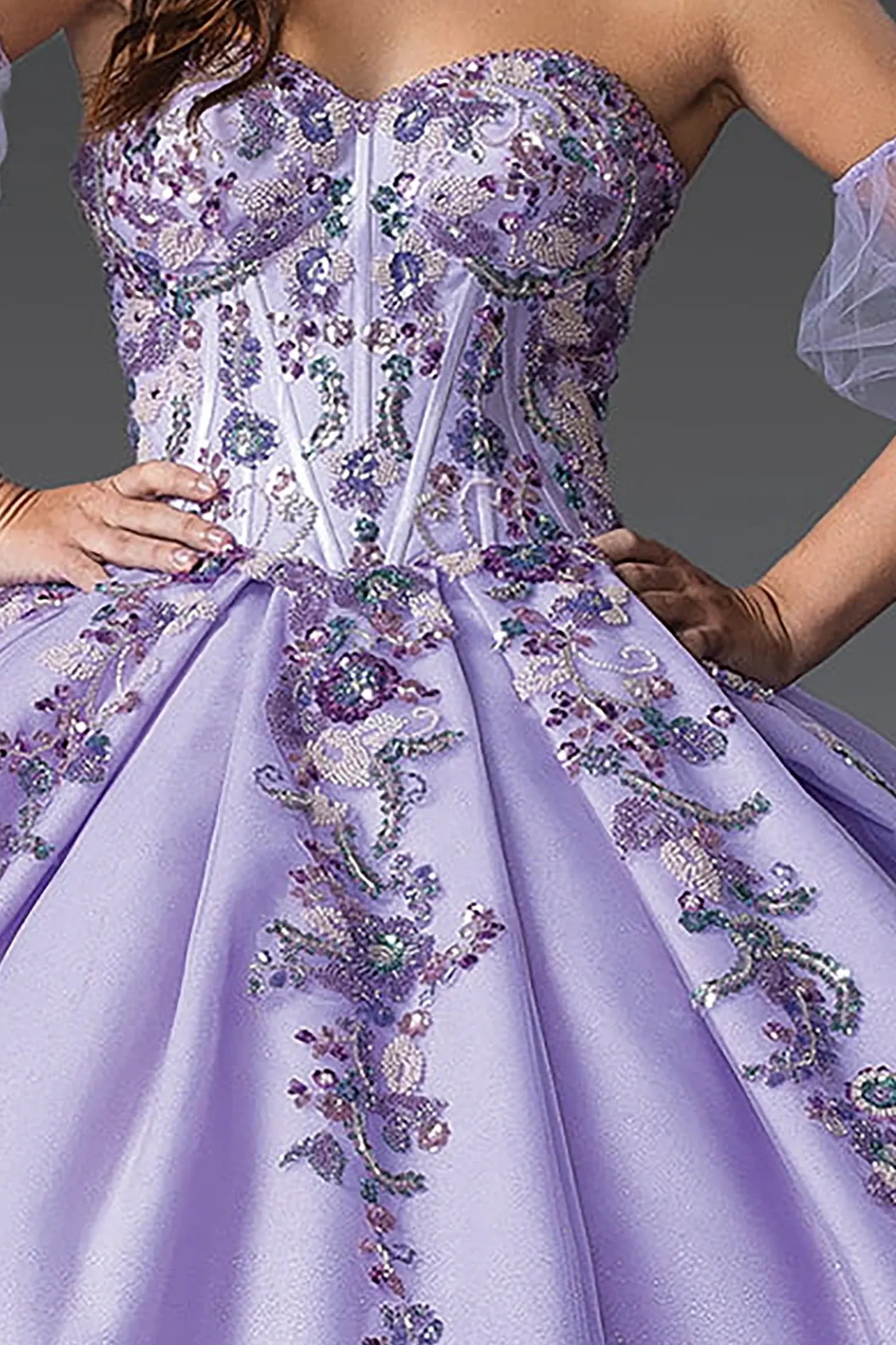 Zoomed front view of a lilac quinceanera dress highlighting floral appliques, glittered bodice, detachable puff sleeves, and layered skirt