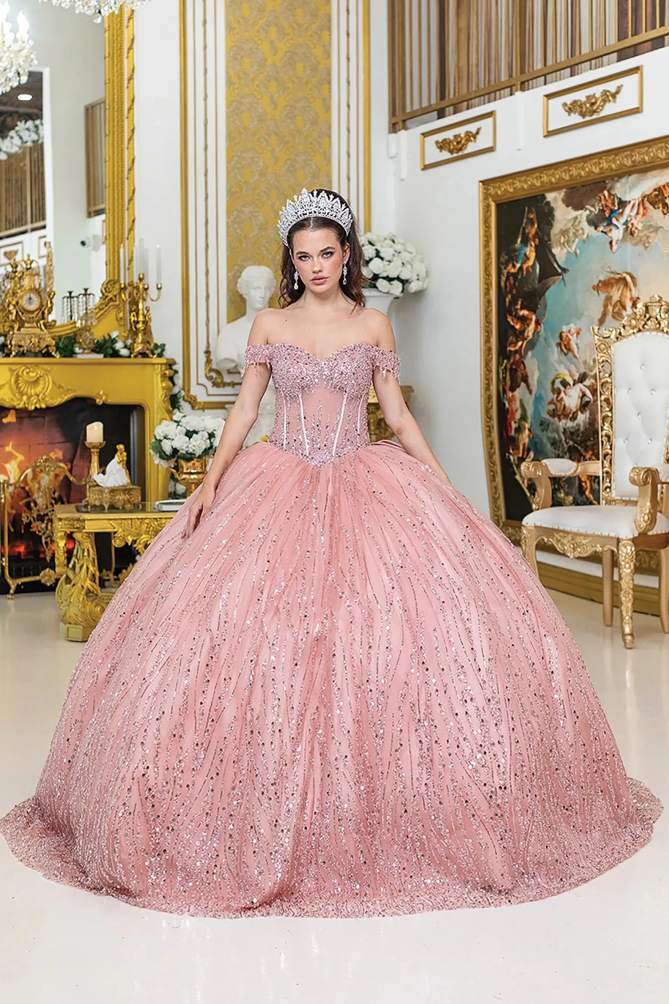 Woman standing front-facing in pink quinceañera ball gown with off-shoulder sleeves, sequined overlay, and intricately beaded bodice