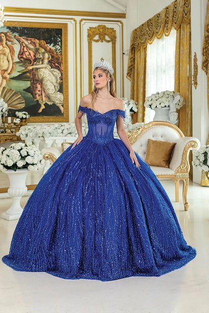 Woman standing front-facing in royal blue quinceañera ball gown with off-shoulder sleeves, sequined overlay, beaded bodice, and layered glittering skirt