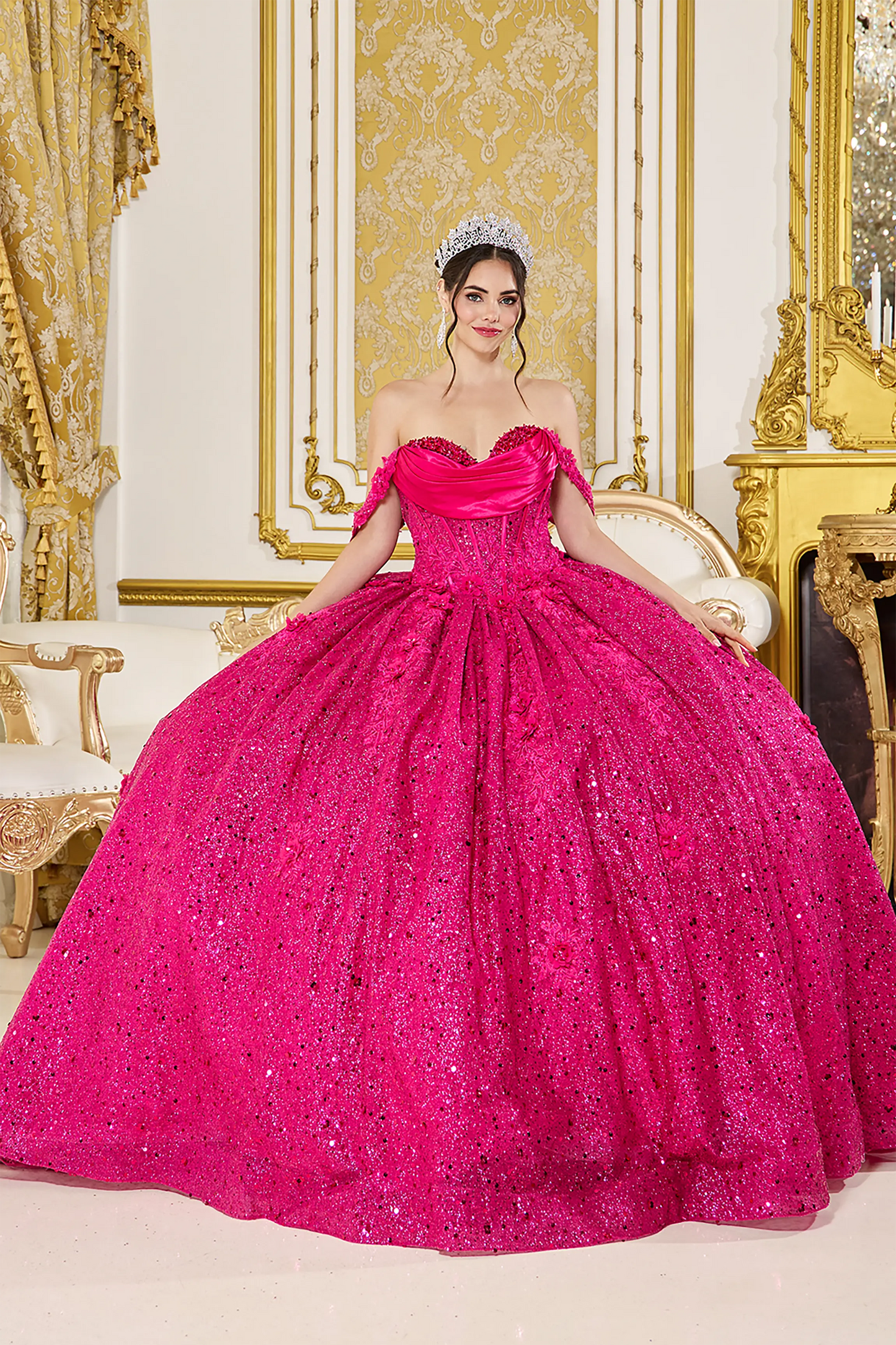 Front view of a woman wearing fuchsia quinceañera dress featuring off-shoulder neckline, ruched bodice, 3D floral appliqué, and glitter tulle skirt