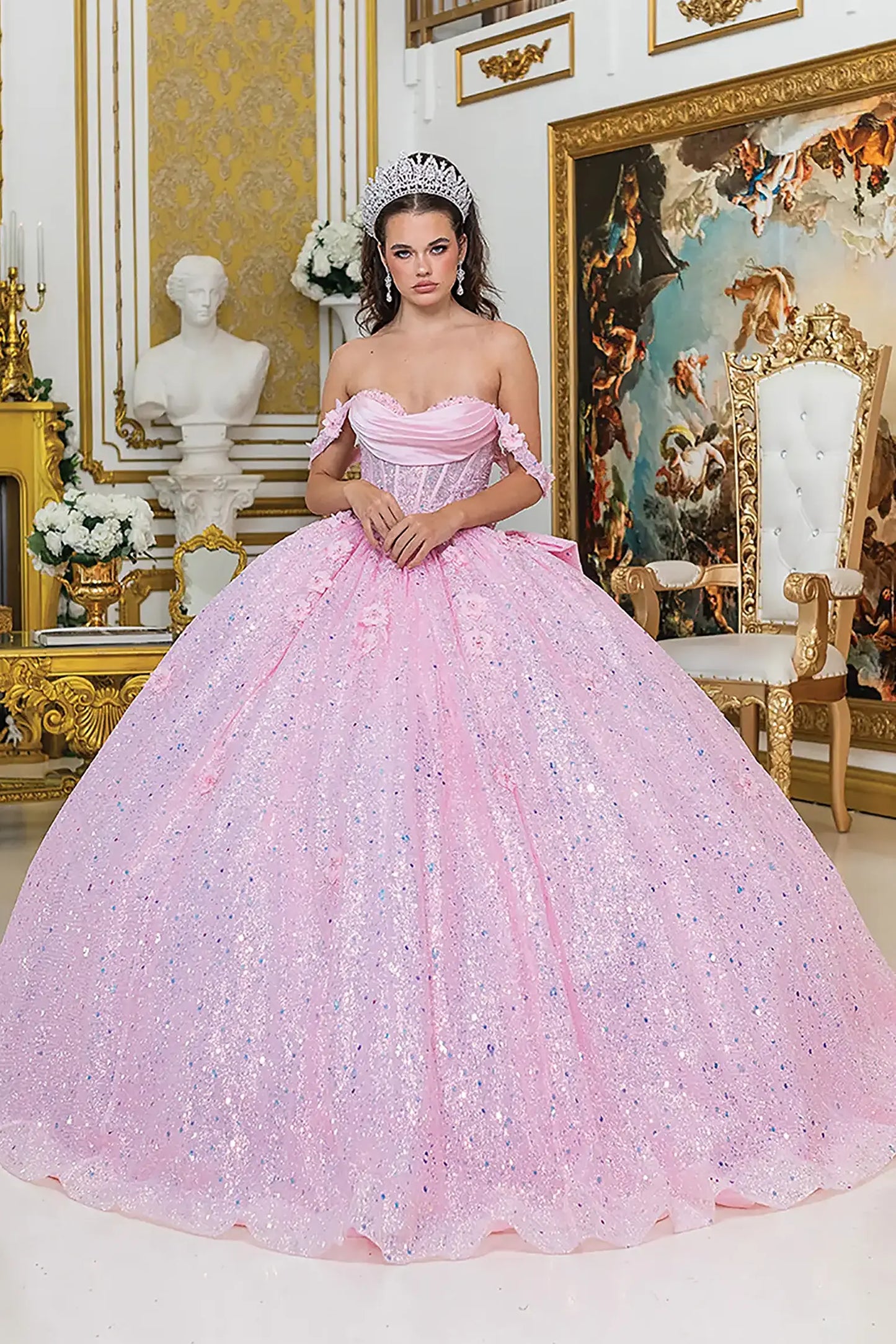 Front view of a woman wearing pink quinceañera dress featuring off-shoulder neckline, ruched bodice, 3D floral appliqué, and glitter tulle skirt