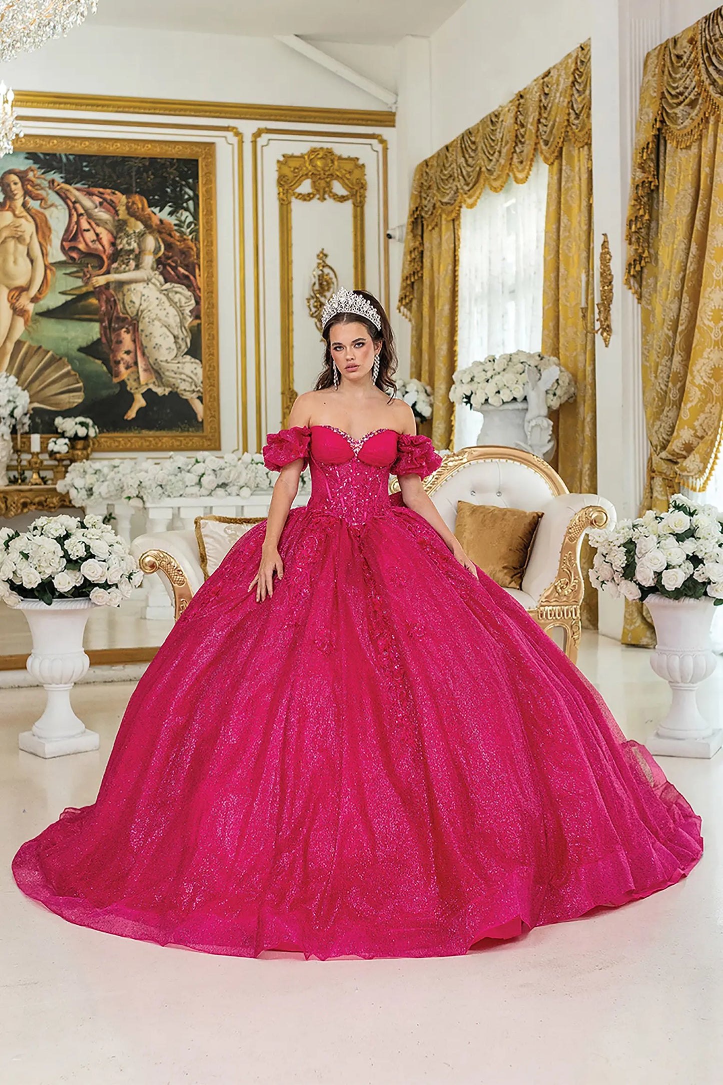 Woman standing front-facing in fuchsia quinceañera ball gown with off-shoulder ruffled sleeves, embroidered bodice, and voluminous sparkling skirt