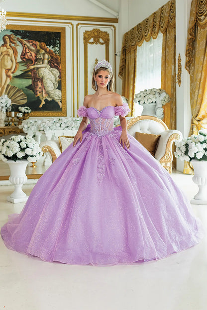 Woman standing front-facing in lilac quinceañera ball gown with off-shoulder sleeves, embroidered bodice, intricate floral appliqués, and voluminous sparkling skirt