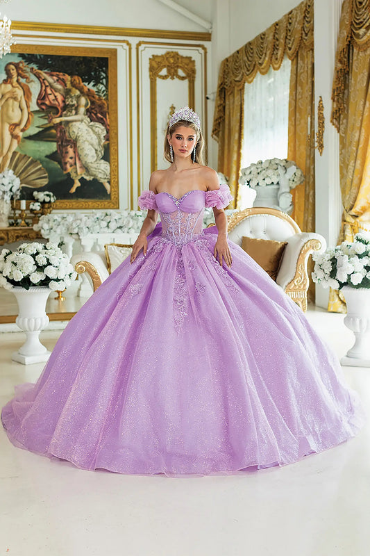Woman standing front-facing in lilac quinceañera ball gown with off-shoulder sleeves, embroidered bodice, intricate floral appliqués, and voluminous sparkling skirt